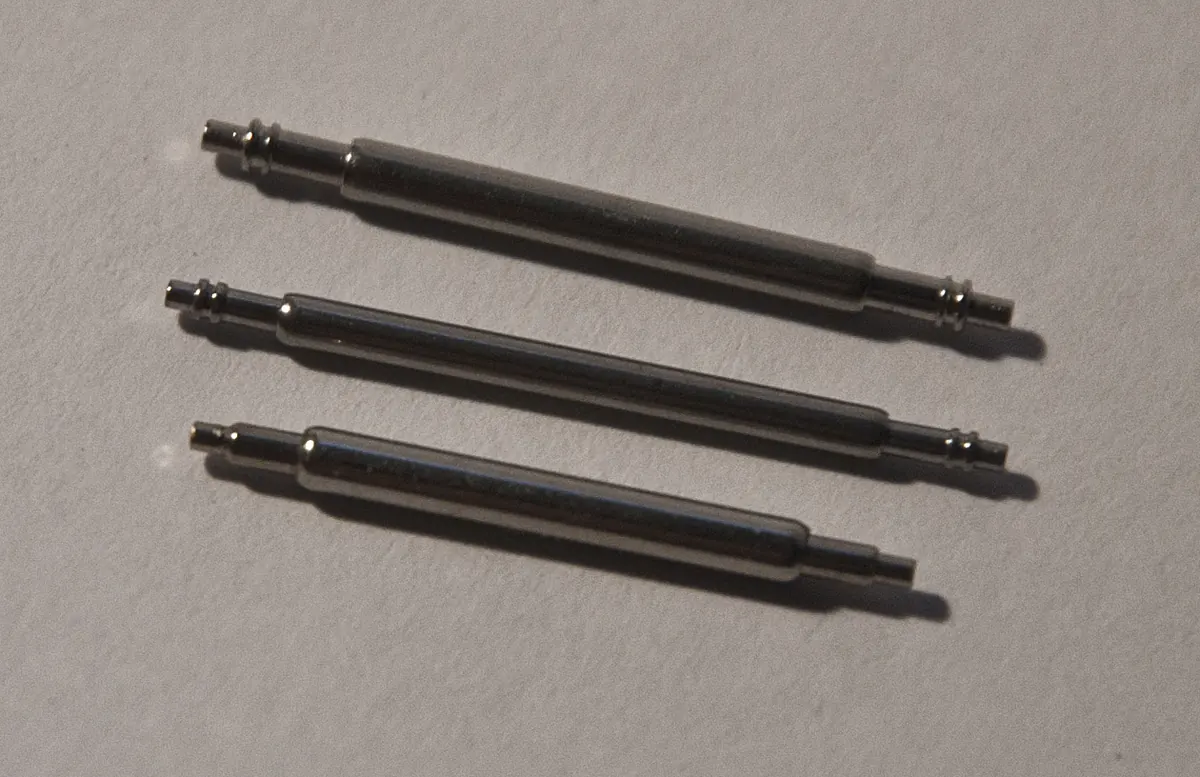 Three steel watch spring bars on a gray surface